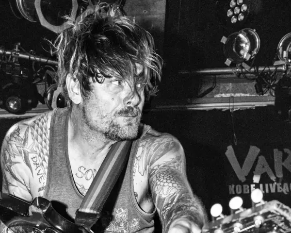 Un guitariste tatoué, cheveux en bataille, sous les projecteurs du VART. Kobe Liveact Bar.