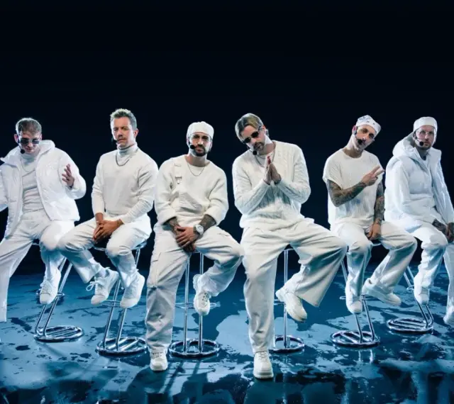 Six hommes en tenue blanche, assis sur des tabourets, évoquant l'univers des albums de Electric Callboy.