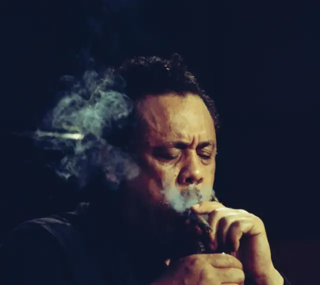 Charlie Mingus, le légendaire contrebassiste, exhale une fumée épaisse, les yeux clos, absorbé par sa musique.