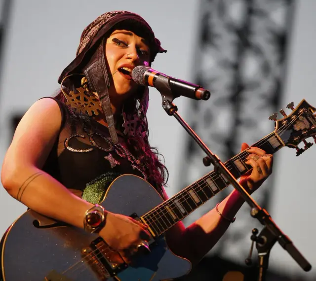 Une artiste de Hiatus Kaiyote, casquette sur la tête, chante et joue de sa guitare bleue étincelante sur scène.