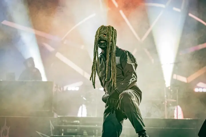 Un membre de Slipknot, masqué et en combinaison, sur scène sous des projecteurs.