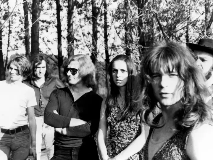 Un groupe rock allemand des années 70, avec des membres aux cheveux longs et des tenues décontractées, posant devant des arbres.