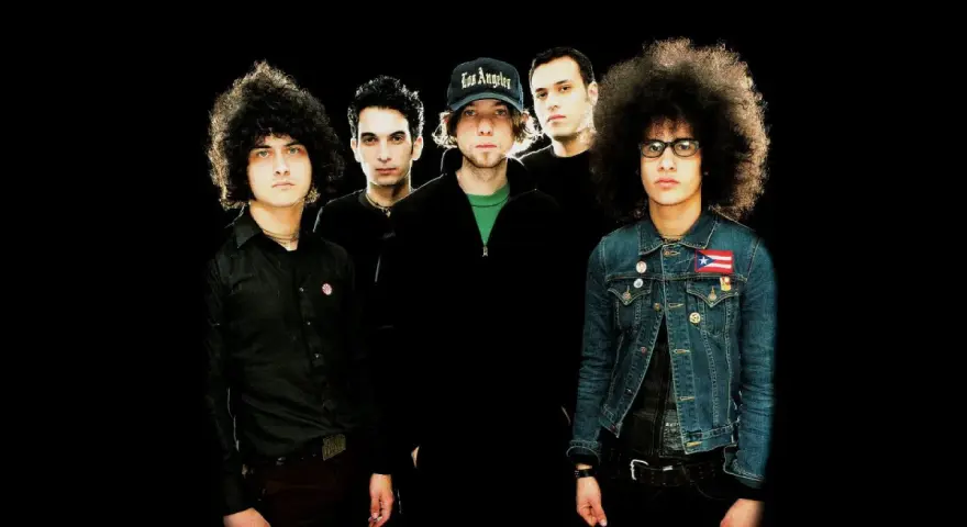 Cinq musiciens, dont certains avec des coiffures afro, posent pour une photo de groupe. L'un porte une casquette "Los Angeles". Ils sont prêts pour une soirée **at the drive in**.