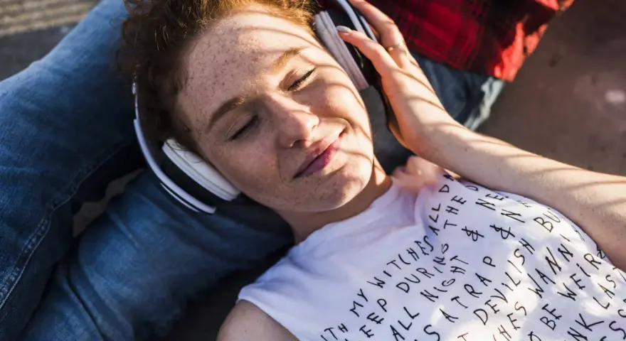 Jeune femme aux taches de rousseur, écouteurs blancs, profitant de la musique. Le volume est à 95 db équivalent, elle semble détendue.