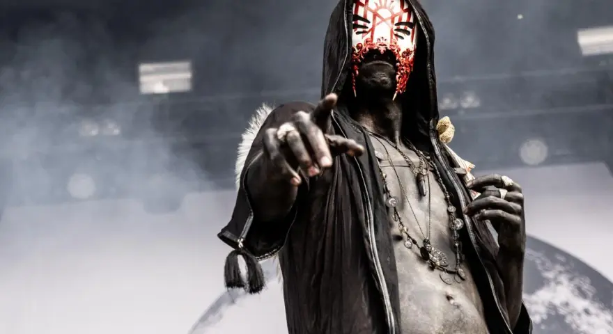 Un membre d'un groupe metal masqué, le visage peint de rouge et blanc, pointe du doigt.