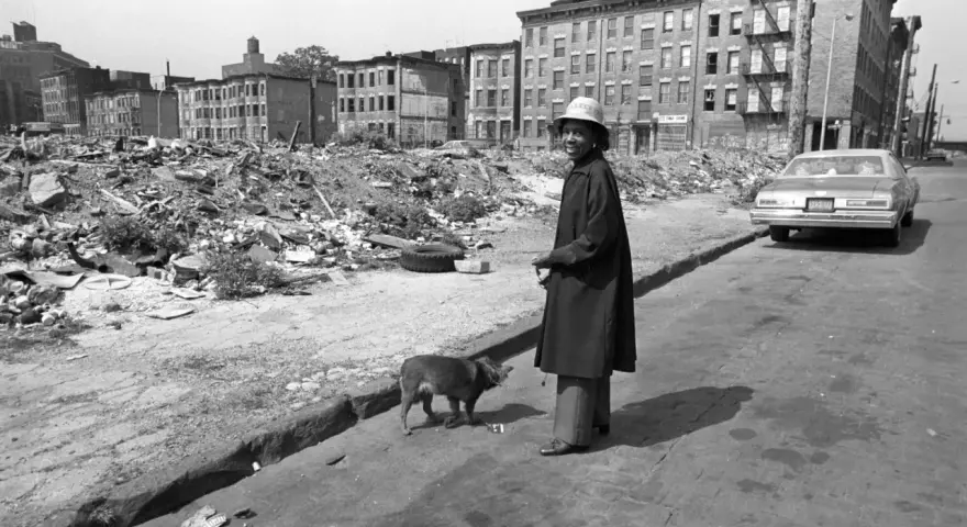 Une femme et son chien devant des immeubles délabrés et des décombres.