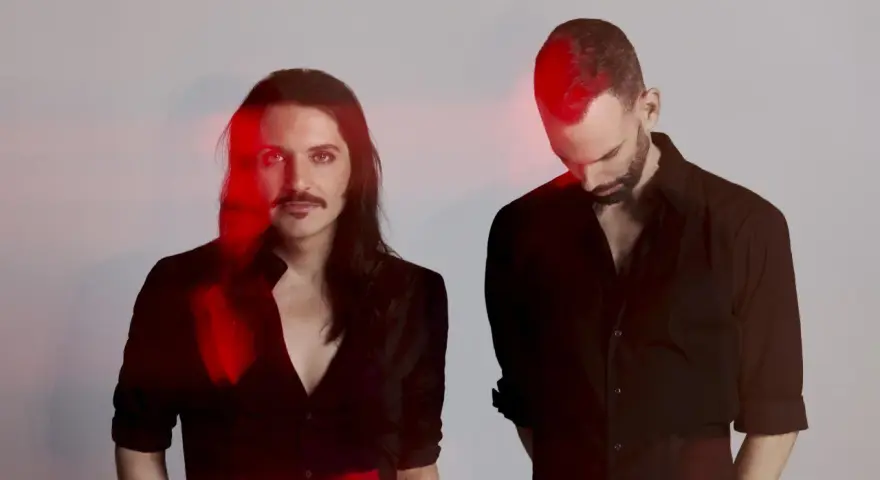 Les membres de Placebo, Brian Molko et Stefan Olsdal, posent en noir et blanc avec des éclats de lumière rouge.