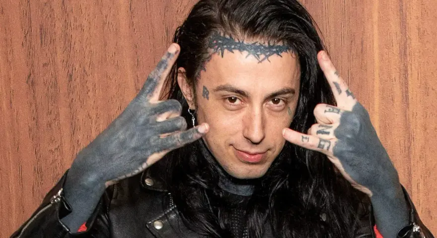 Un membre de Falling In Reverse, avec des tatouages sur le visage et les mains, fait le signe des cornes.