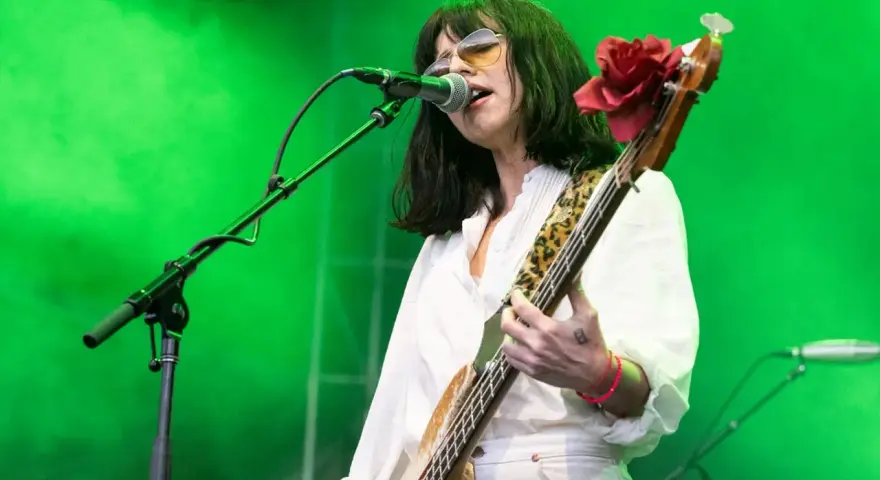 La chanteuse des Pixies, Kim Deal, joue de la basse sur scène, éclairée par une lumière verte.
