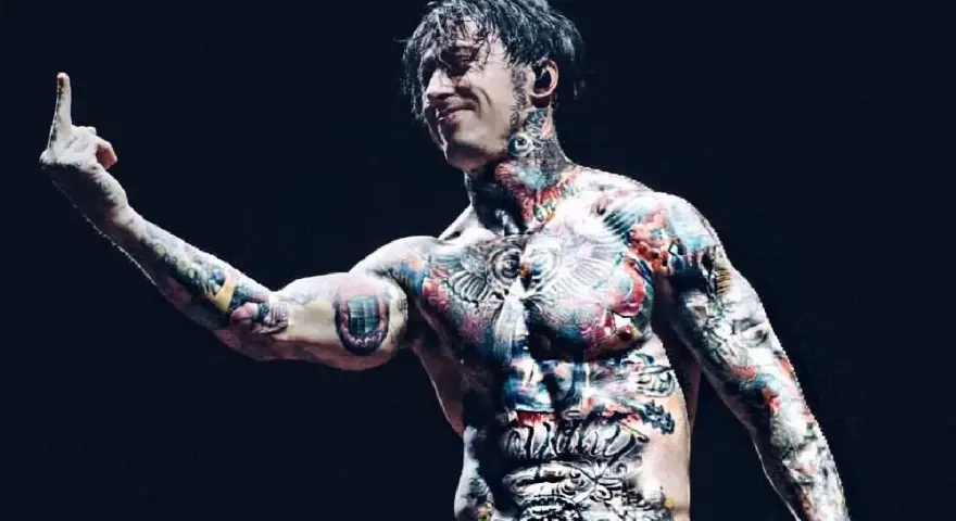 Le chanteur de Falling In Reverse, Ronnie Radke, torse nu et couvert de tatouages colorés, lève le majeur sur scène.