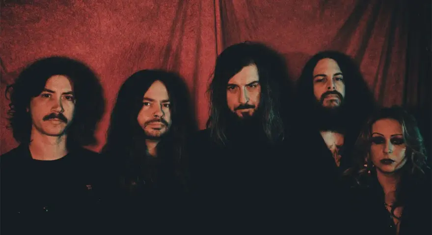 Cinq membres du groupe Uncle Acid and the Deadbeats posent devant un rideau rouge.