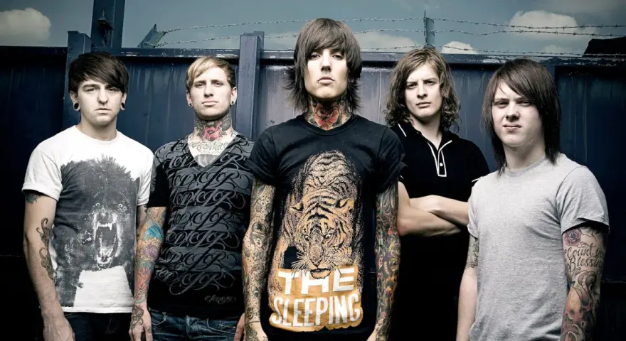 Cinq membres du groupe Bring Me The Horizon posent devant une clôture. Le chanteur porte un t-shirt avec un tigre et le texte "The Sleeping".