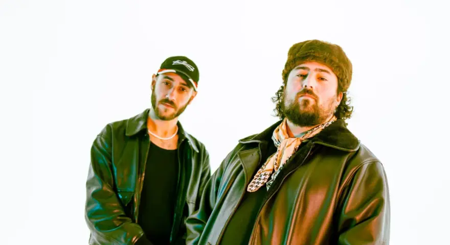 Deux DJ les plus connus, l'un porte une casquette et l'autre un bonnet en fourrure, posent devant un fond blanc.
