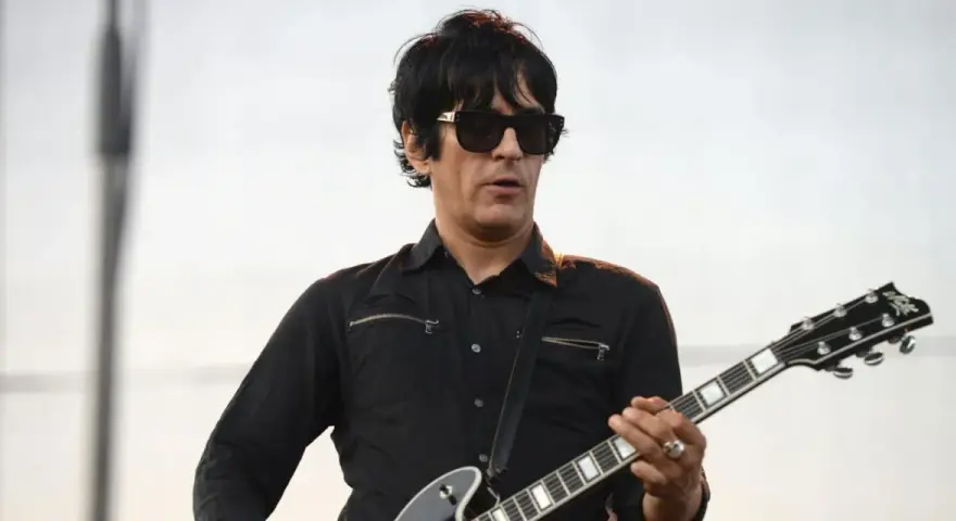 Un des membres de Eagles of Death Metal, guitariste en chemise noire et lunettes de soleil, joue sur scène.