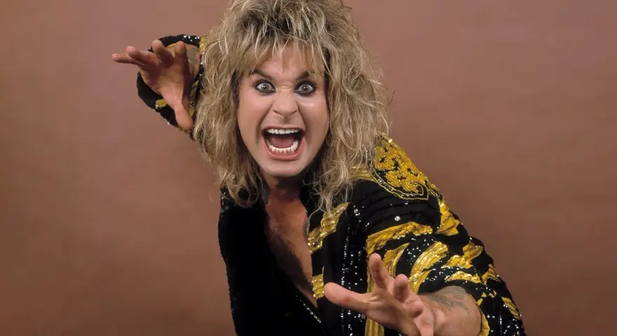 Ozzy Osbourne, le prince des ténèbres, avec sa chevelure blonde ébouriffée et un regard intense, porte une veste noire ornée de motifs dorés.