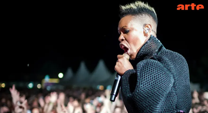 Skunk Anansie en pleine performance, micro d'or à la main, devant une foule en délire. La chanteuse captive avec son énergie.
