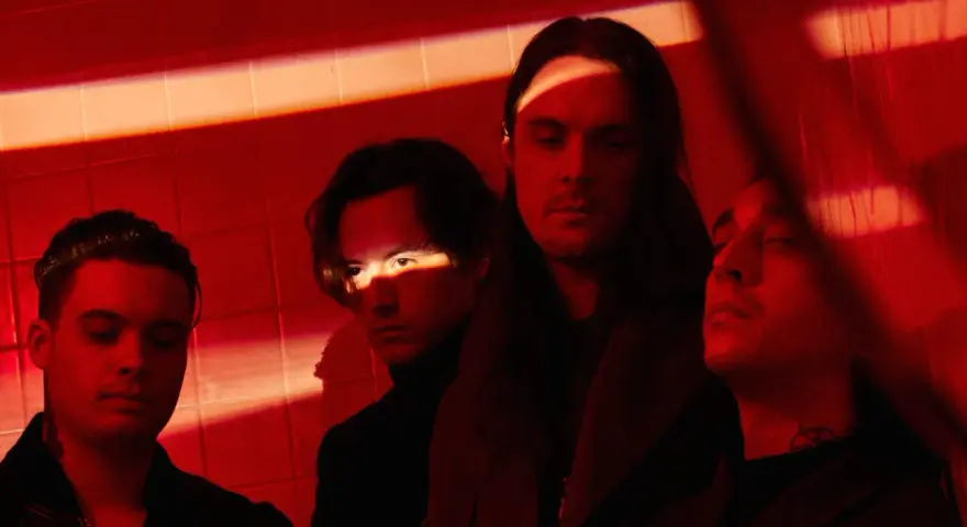 Les membres de Bad Omens posent dans une ambiance rouge intense, éclairés par des ombres dramatiques.