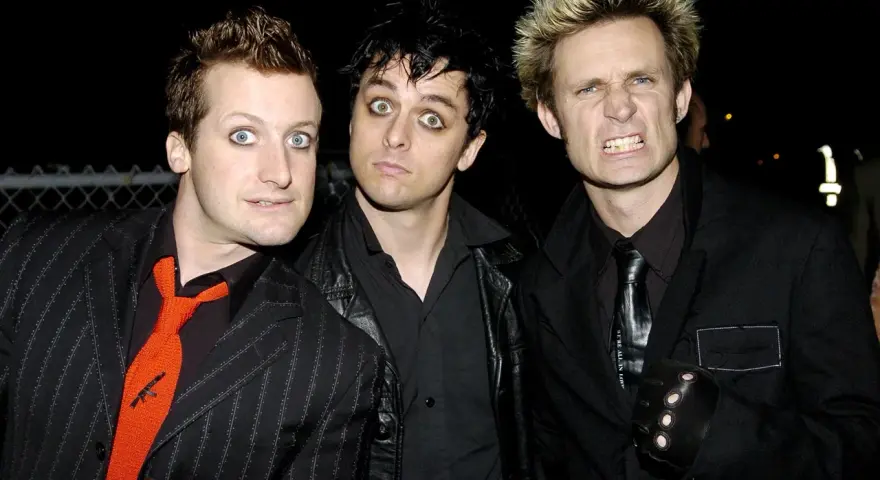 Les membres de Green Day, Billie Joe Armstrong, Mike Dirnt et Tré Cool, posent ensemble. Armstrong a les yeux écarquillés, Dirnt a un regard intense et Cool fait une grimace.