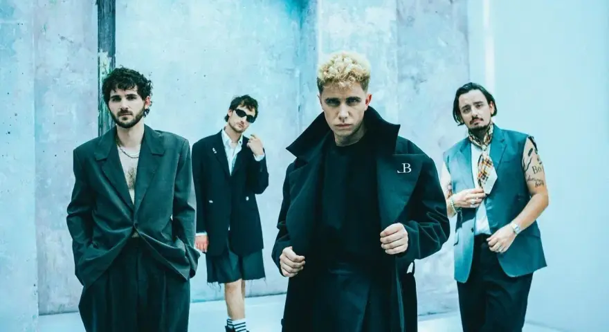 Le groupe Last Train pose devant un mur bleu clair, quatre hommes aux styles audacieux.