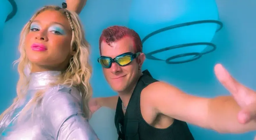 Un groupe hollandais des années 90, avec une femme au maquillage bleu vif et un homme aux lunettes futuristes, pose devant des sphères lumineuses bleues.