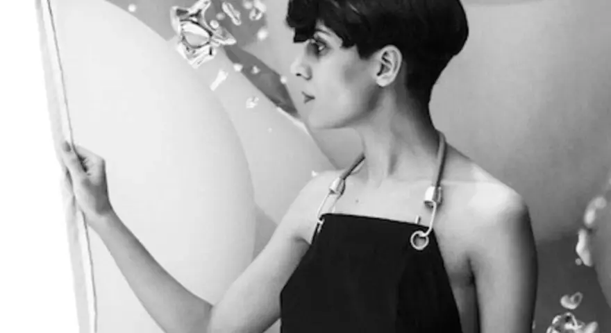 Fatima Al Qadiri, artiste à la coupe courte, porte un tablier noir, regardant une œuvre abstraite.
