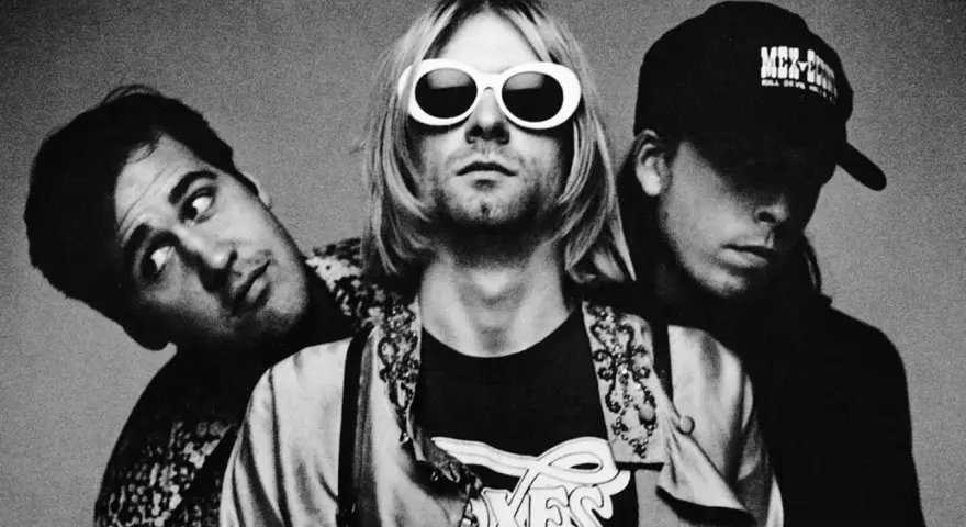 Les membres de Nirvana posent ensemble, Kurt Cobain au centre avec ses lunettes blanches iconiques.