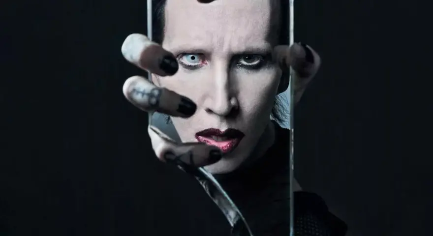 Marilyn Manson, visage décomposé dans un miroir brisé, évoquant l'esthétique sombre de ses albums.