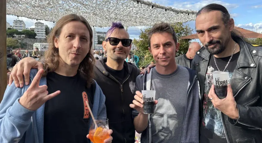 Quatre hommes, un groupe hollandais des années 80, posent avec des boissons. L'un fait un signe de rock.