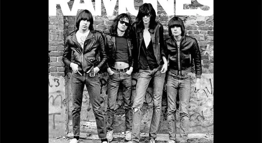 Les Ramones, quatre icônes punk en blousons de cuir et jeans, posent devant un mur de briques tagué.