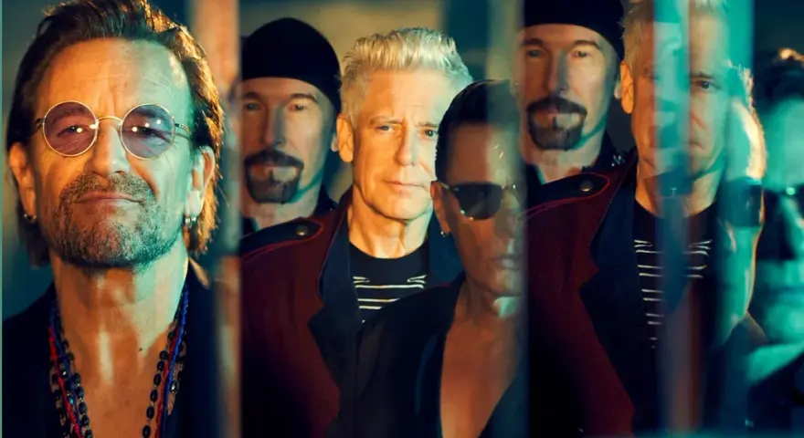 Le groupe U2, avec Bono au premier plan, pose en groupe, leurs visages reflétant une lumière tamisée.