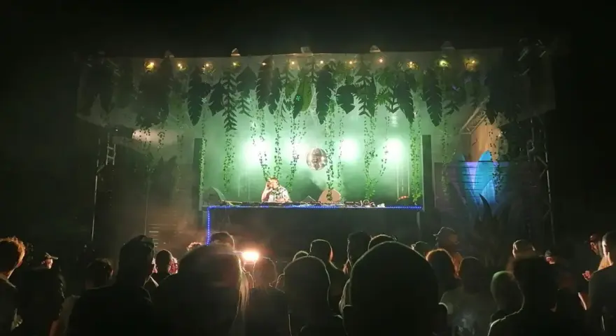 Une dj femme française enflamme la foule sous une décoration jungle. Lumières vertes, fumée et boule à facettes créent une ambiance festive.
