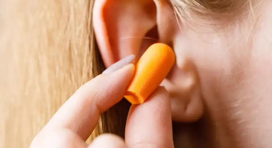 Une main insère une boule quies orange dans une oreille pour réduire les décibels.