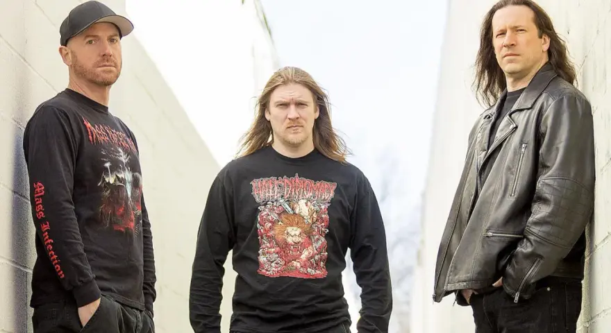 Trois hommes posent devant un mur. L'un porte un t-shirt avec une image de fœtus mourant.