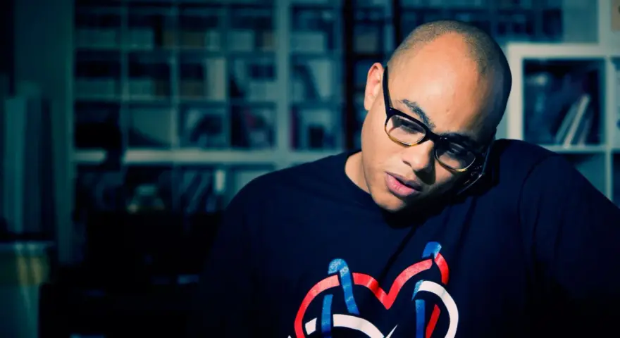 Un homme chauve avec des lunettes, parlant au téléphone, porte un t-shirt avec un logo coloré. Il pourrait bien être celui qui a inventé le rap.
