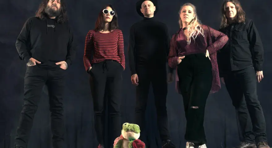 Cinq personnes se tiennent devant un fond sombre. Au premier plan, une grenouille en peluche tient une rose. Le groupe, comme un **crippled black phoenix**, semble prêt à s'envoler.