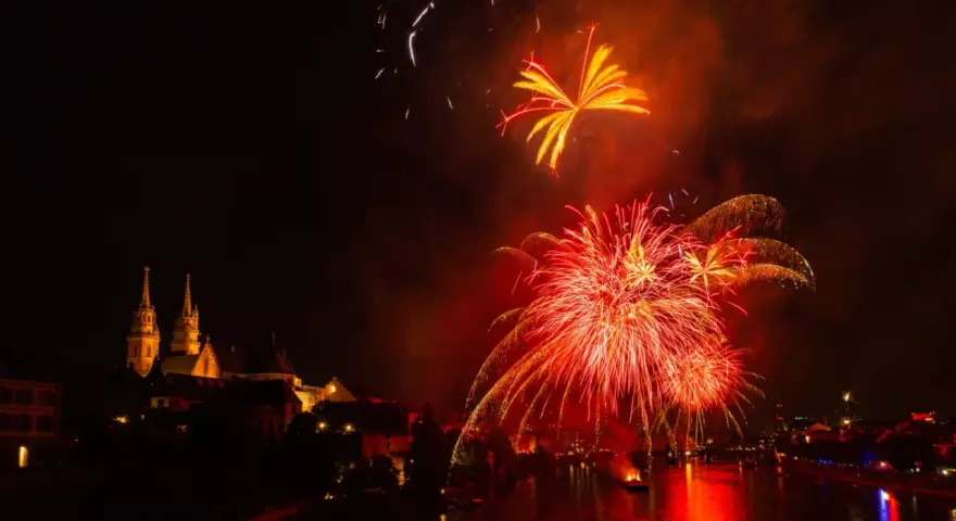 Feu d'artifice rougeoyant illuminant le ciel nocturne au-dessus d'une ville et d'une rivière. Le **décibel feu d'artifice** résonne dans l'air.