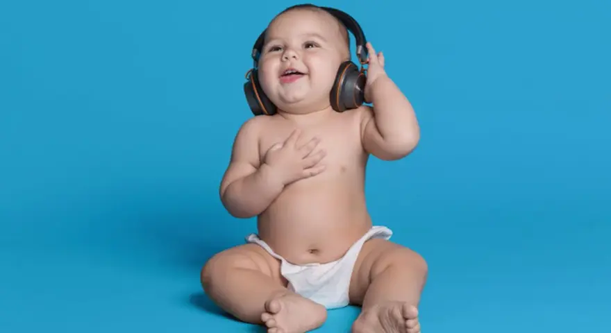 Un bébé souriant, en couche, écoute de la musique avec des écouteurs, le décibel maximum pour un bébé est à éviter.