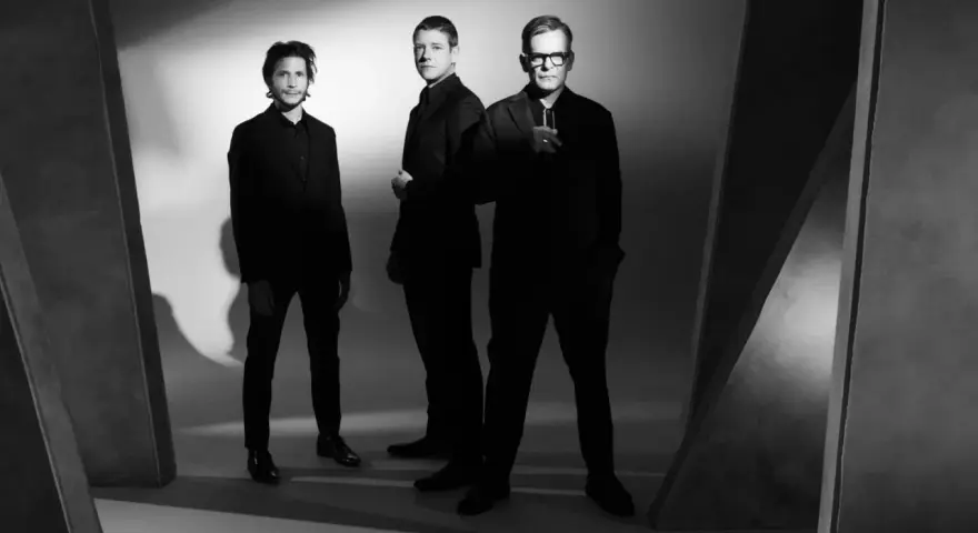 Le groupe Interpol pose en noir et blanc, trois hommes en costumes sombres, dans une ambiance épurée et artistique.