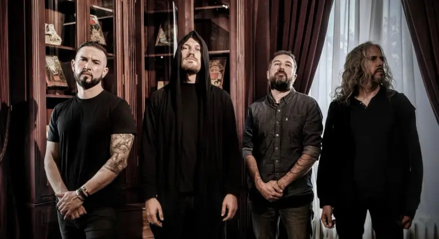 Quatre musiciens, dont un avec une capuche, posent devant des étagères remplies de livres. Ce groupe metal français connu dégage une aura mystérieuse.