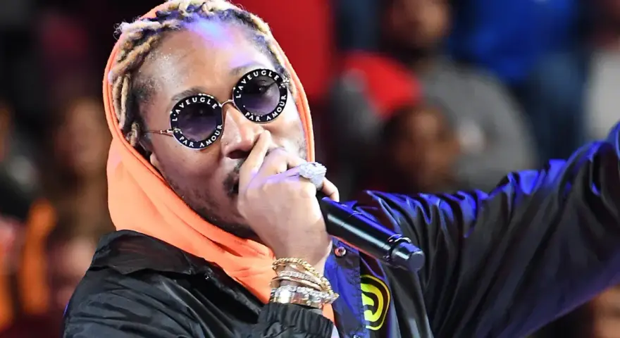 Un rappeur à la mode, avec des lunettes stylées et de nombreux bijoux, chante sur scène.