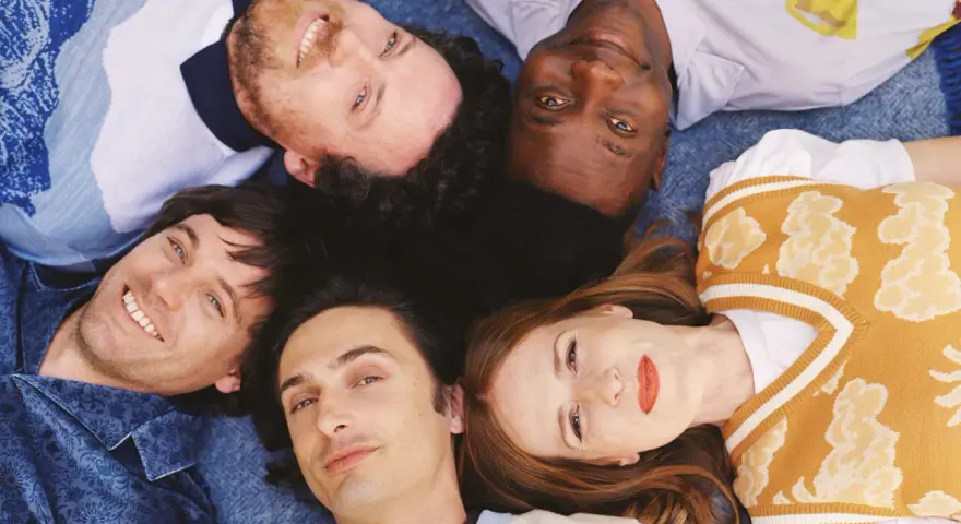 Les membres de Metronomy, cinq visages souriants, forment une étoile sur un fond bleu.
