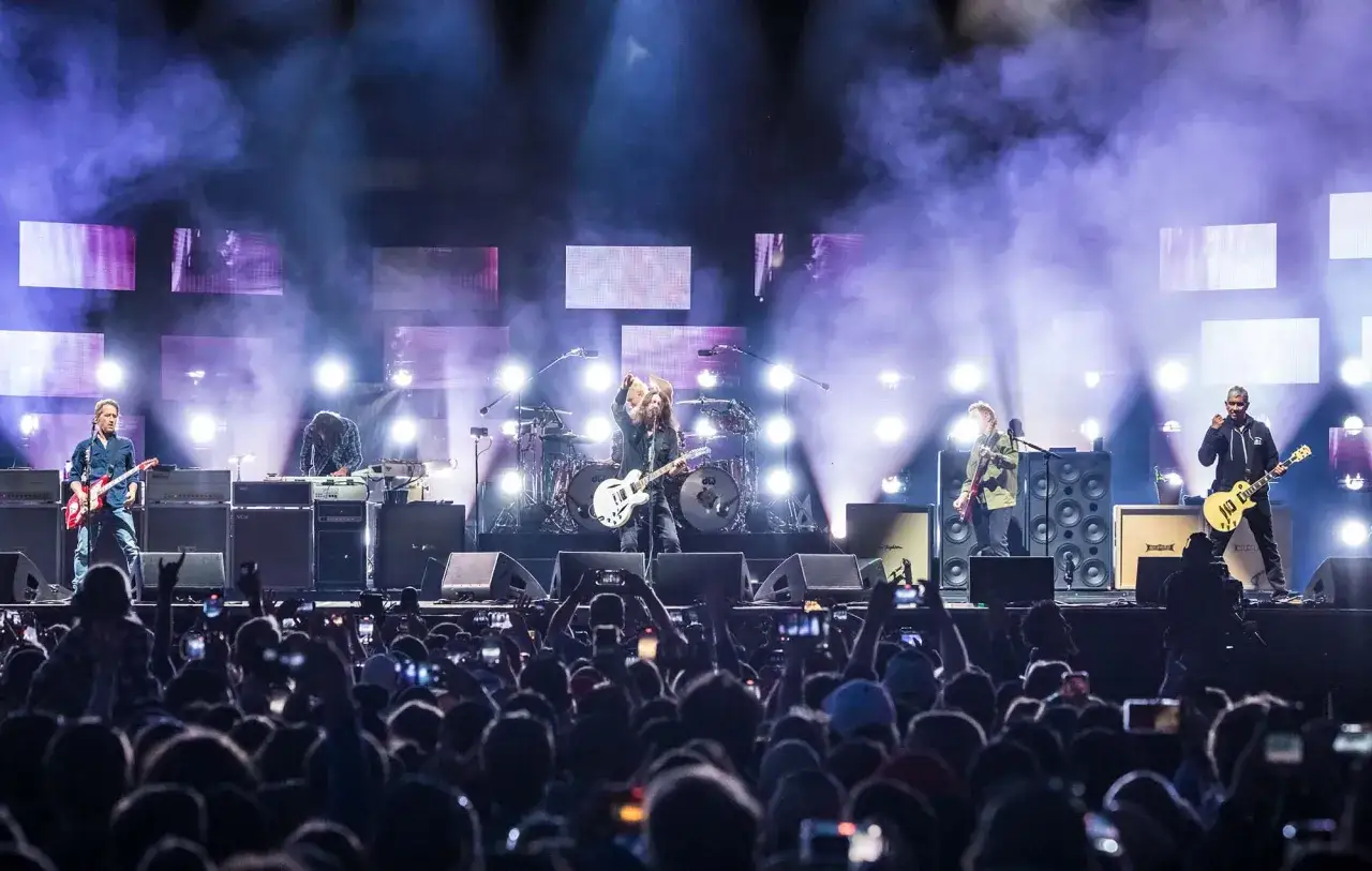 Le groupe Foo Fighters en concert, éclairé par des projecteurs, devant une foule en délire.