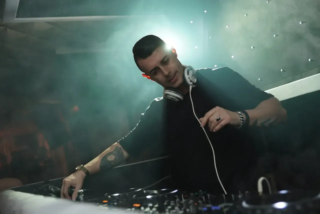 Un artiste deep house mixe dans une ambiance enfumée, sous des lumières tamisées.