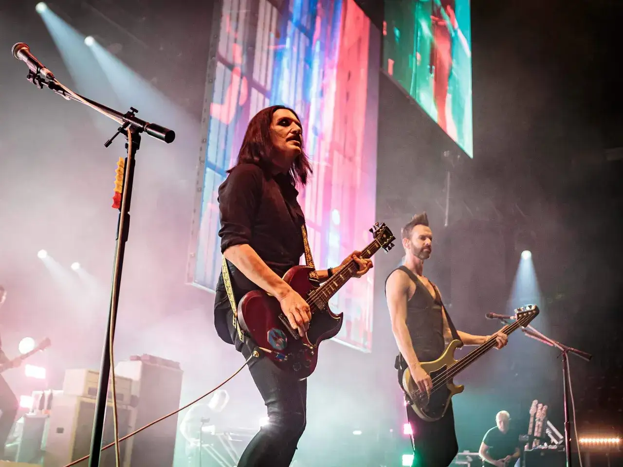 Les membres de Placebo sur scène, Brian Molko à la guitare et Stefan Olsdal à la basse, sous des lumières vives.