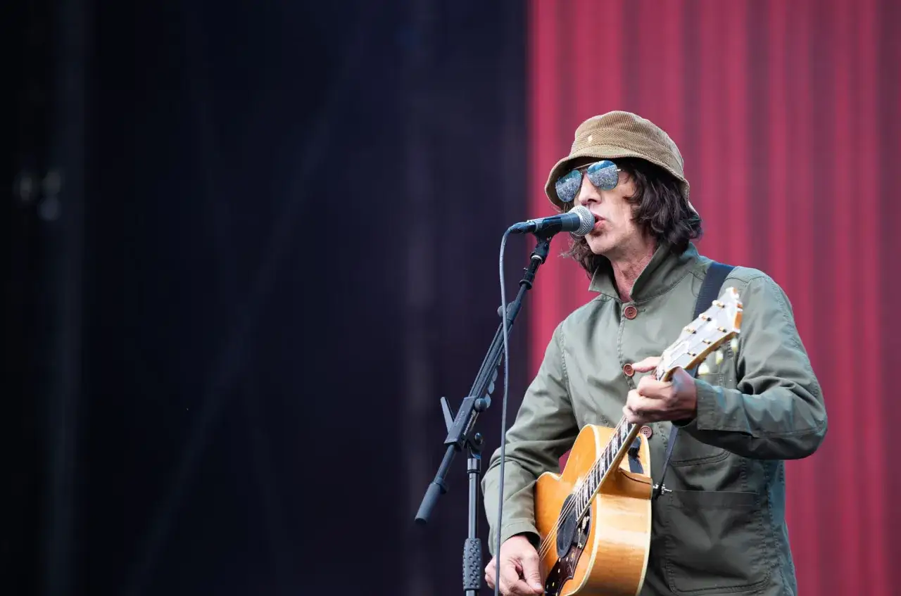 Richard Ashcroft, chanteur de The Verve, joue de la guitare et chante sur sc&egrave;ne, portant un chapeau et des lunettes de soleil.