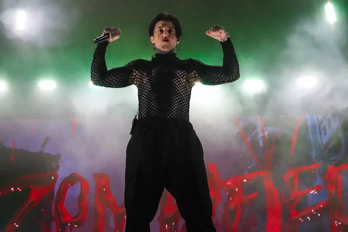 Ronnie Radke, membre de Falling In Reverse, pose sur scène, bras levés, micro en main, sous des lumières vertes et un brouillard.