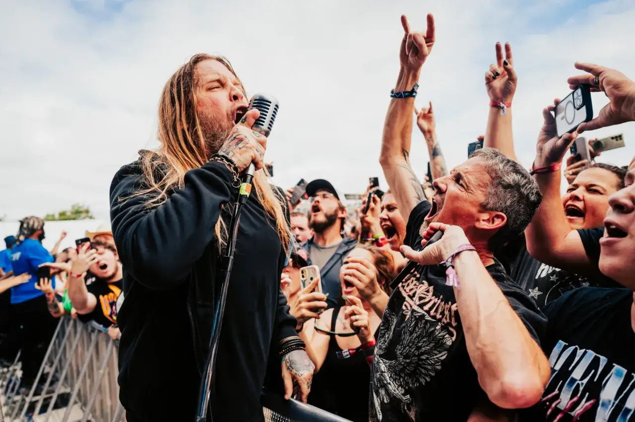 Le chanteur de Drowning Pool hurle dans le micro, entouré d'une foule en délire qui filme le concert avec leurs téléphones.