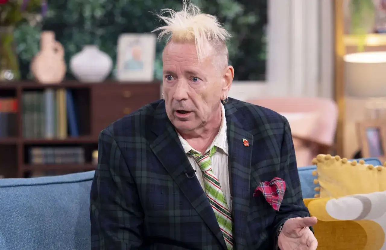 John Lydon, le chanteur des Sex Pistols, avec sa coiffure iconique et un costume à carreaux, parle avec animation.