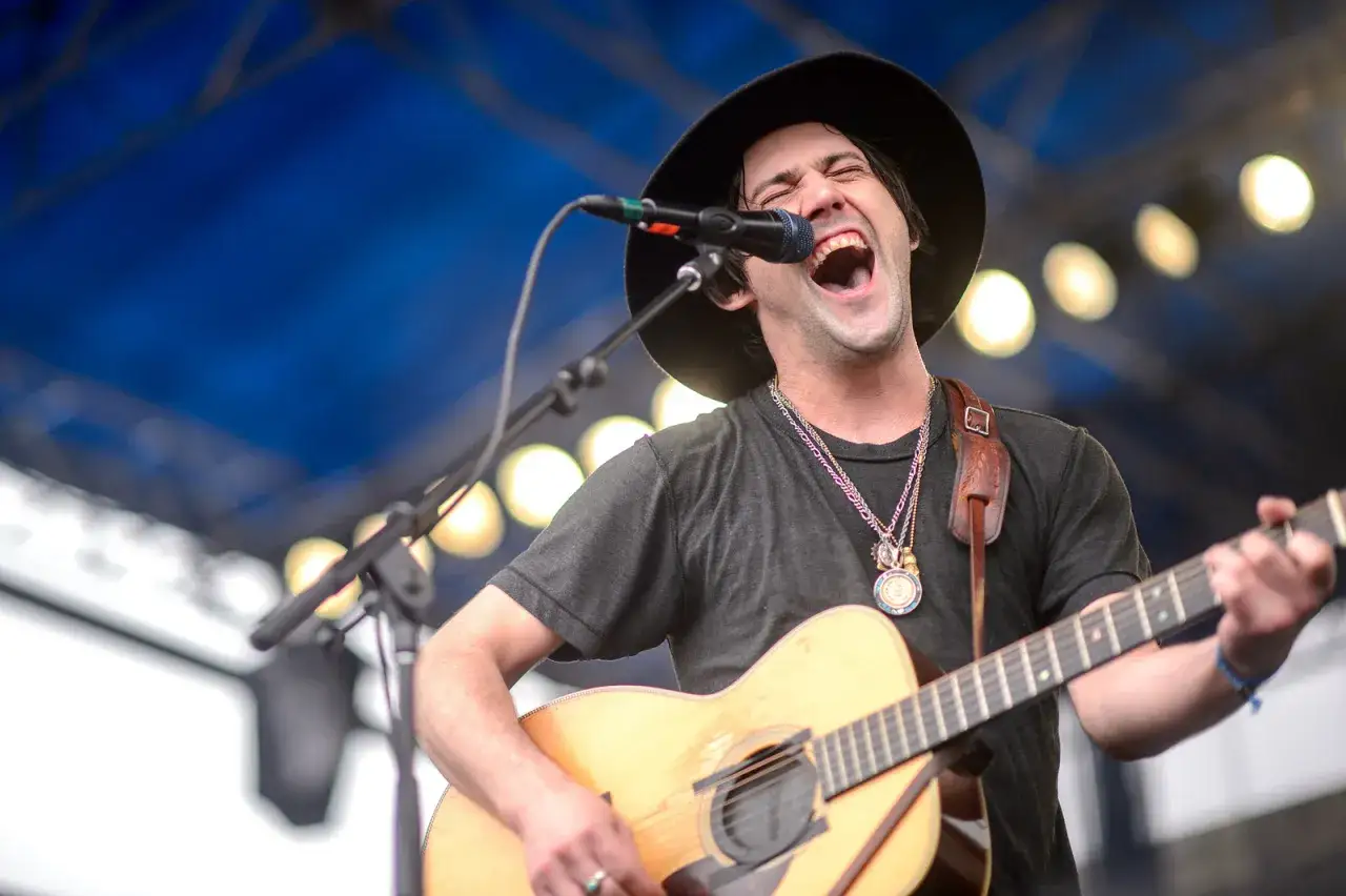 Un chanteur à la guitare, chapeau noir, yeux brillants de passion, chante à pleins poumons sous les lumières.