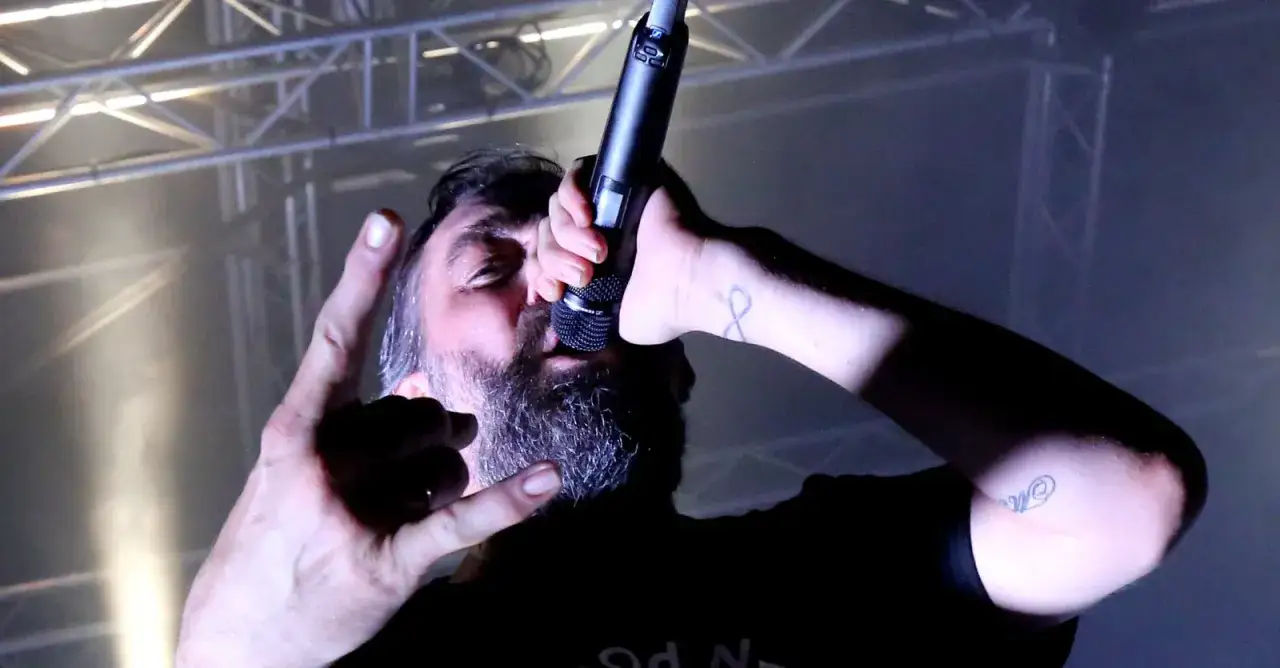 Le chanteur Mass Hysteria, micro en main, fait un signe de rock sur scène.